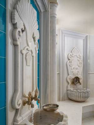 Close-up of an ornate white marble fountain and basin in the Turkish Hammam at Anjana Spa, Rixos Pera Istanbul, set against a wall of vibrant turquoise tiles.