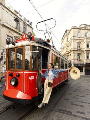 A woman in a light outfit is posing and smiling on the iconic red tram on Istiklal Street in Istanbul, with historic buildings in the background.